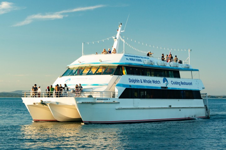Large white boat with people on deck, labeled 'Dolphin & Whale Watch Cruising Restaurant'.