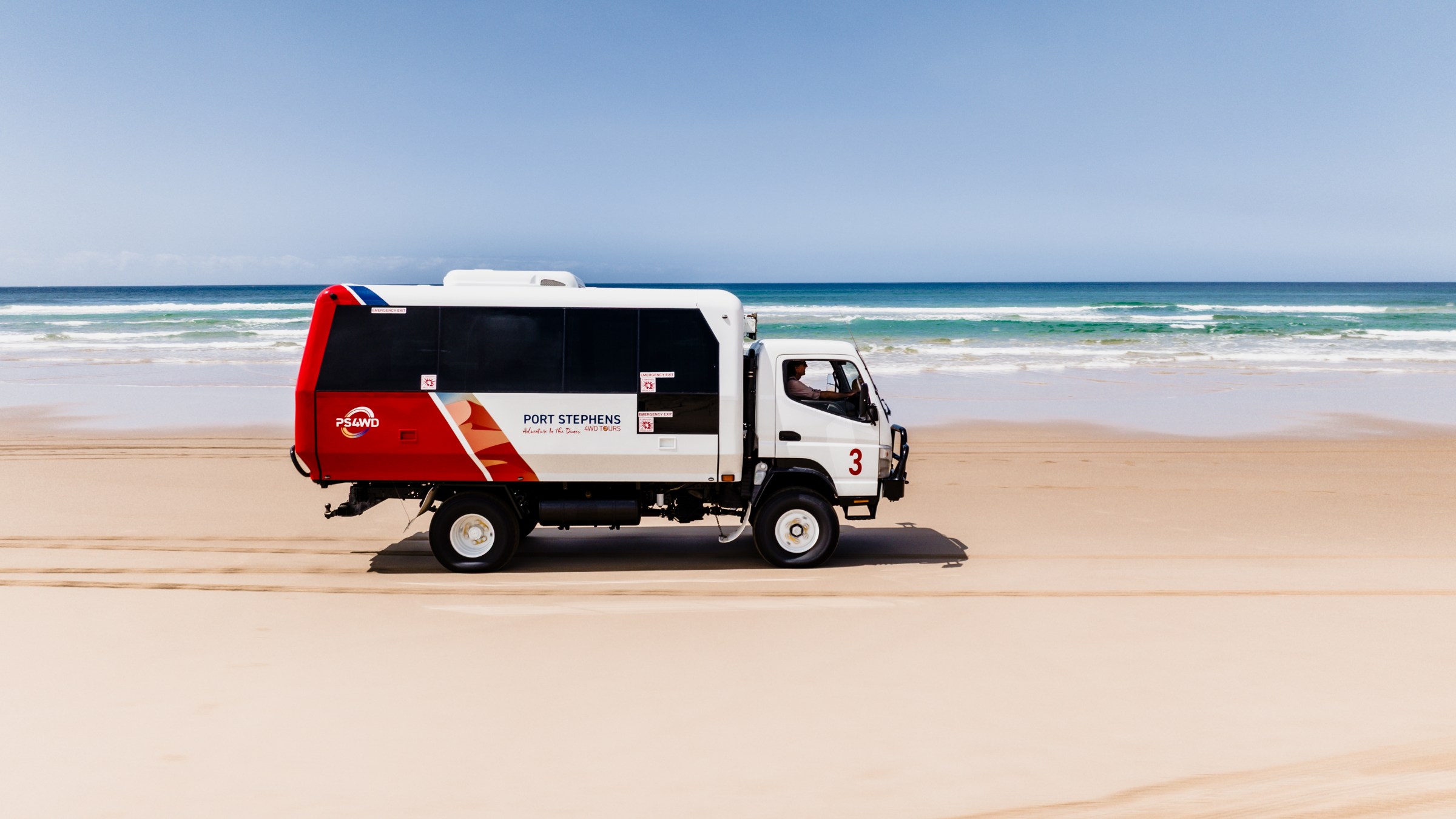 Off-road vehicle driving along a sandy beach with the ocean in the background.