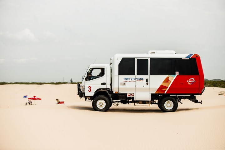 A 4WD vehicle on sand dunes with a red and white design, labeled Port Stephens.